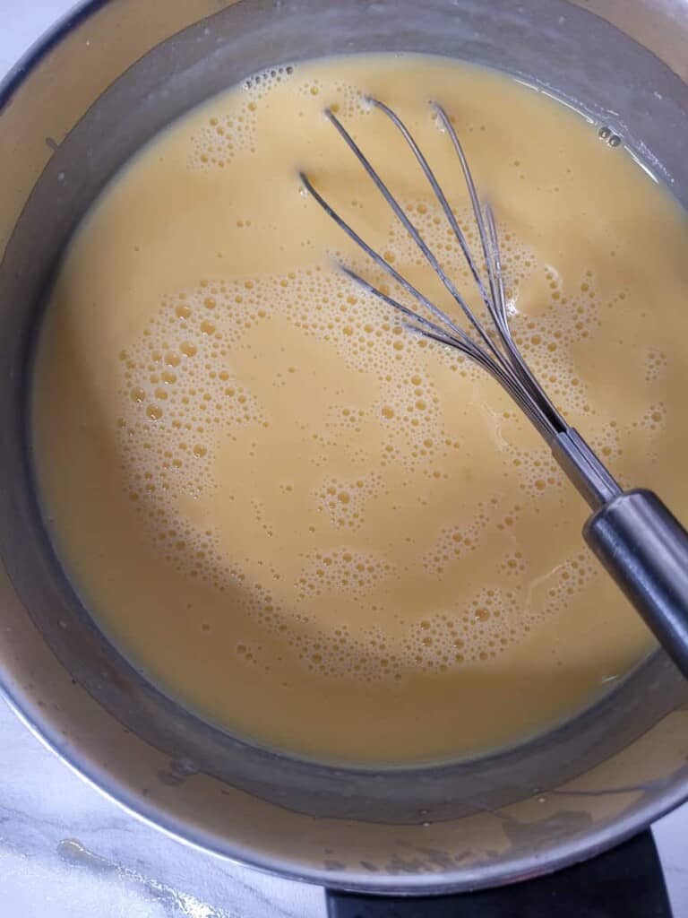 Whisk inside a silve pot with yellow liquid