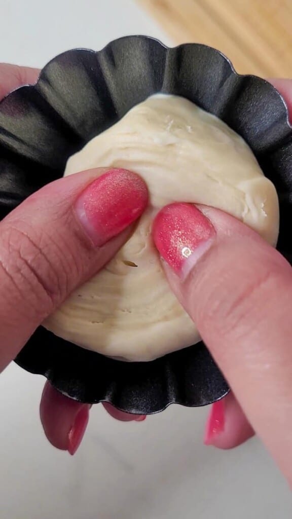 Thumbs pressing pastry dough along a mold