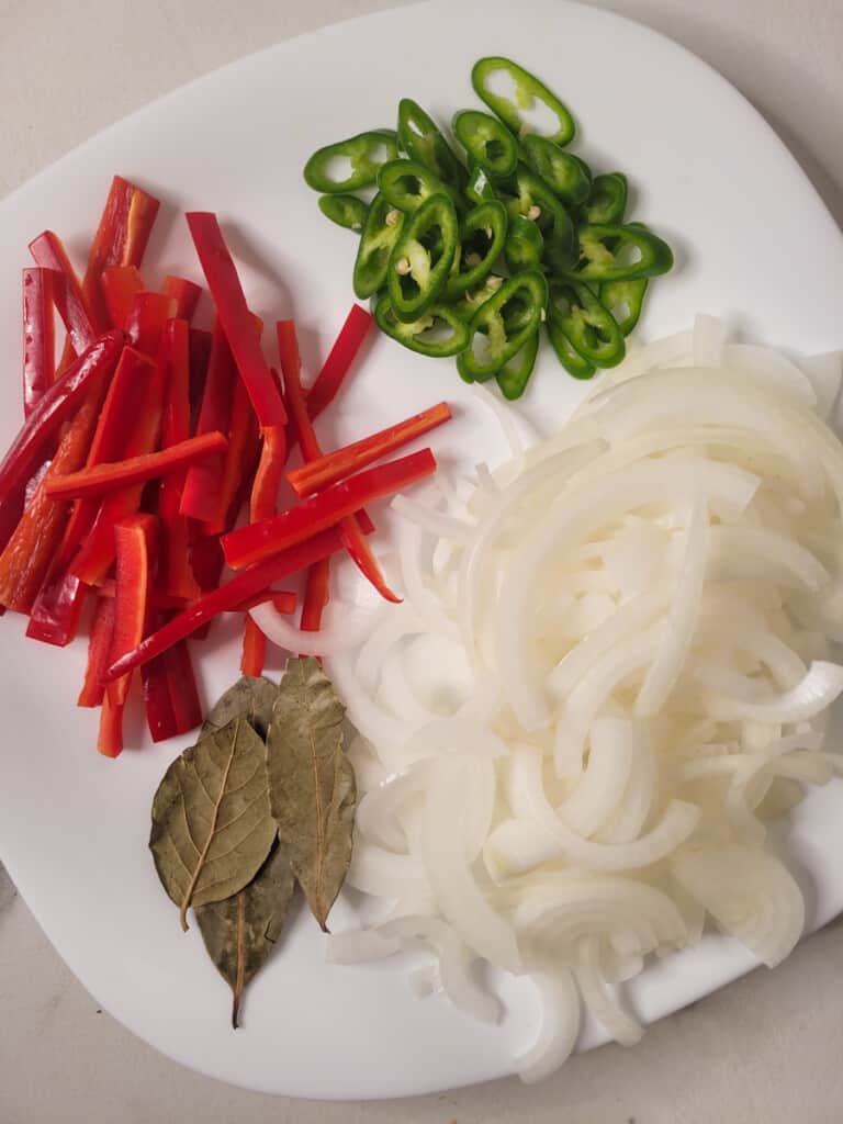A plate of sliced red peppers, green peppers, onions, and bay leaves