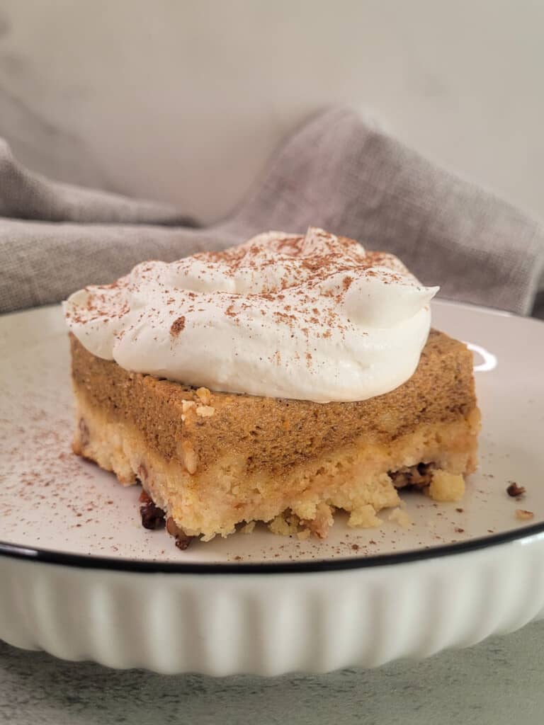 A slice of pumpkin crunch cake with whipped cream on a white plate
