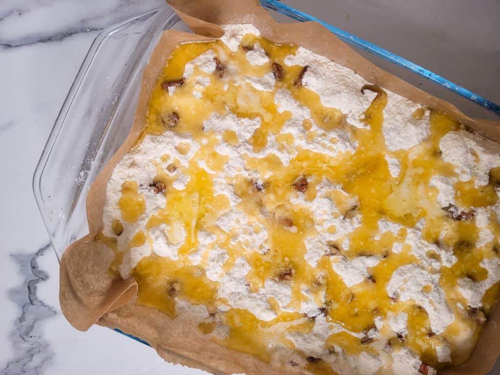 Butter on top of cake mix with pecans in a glass baking dish