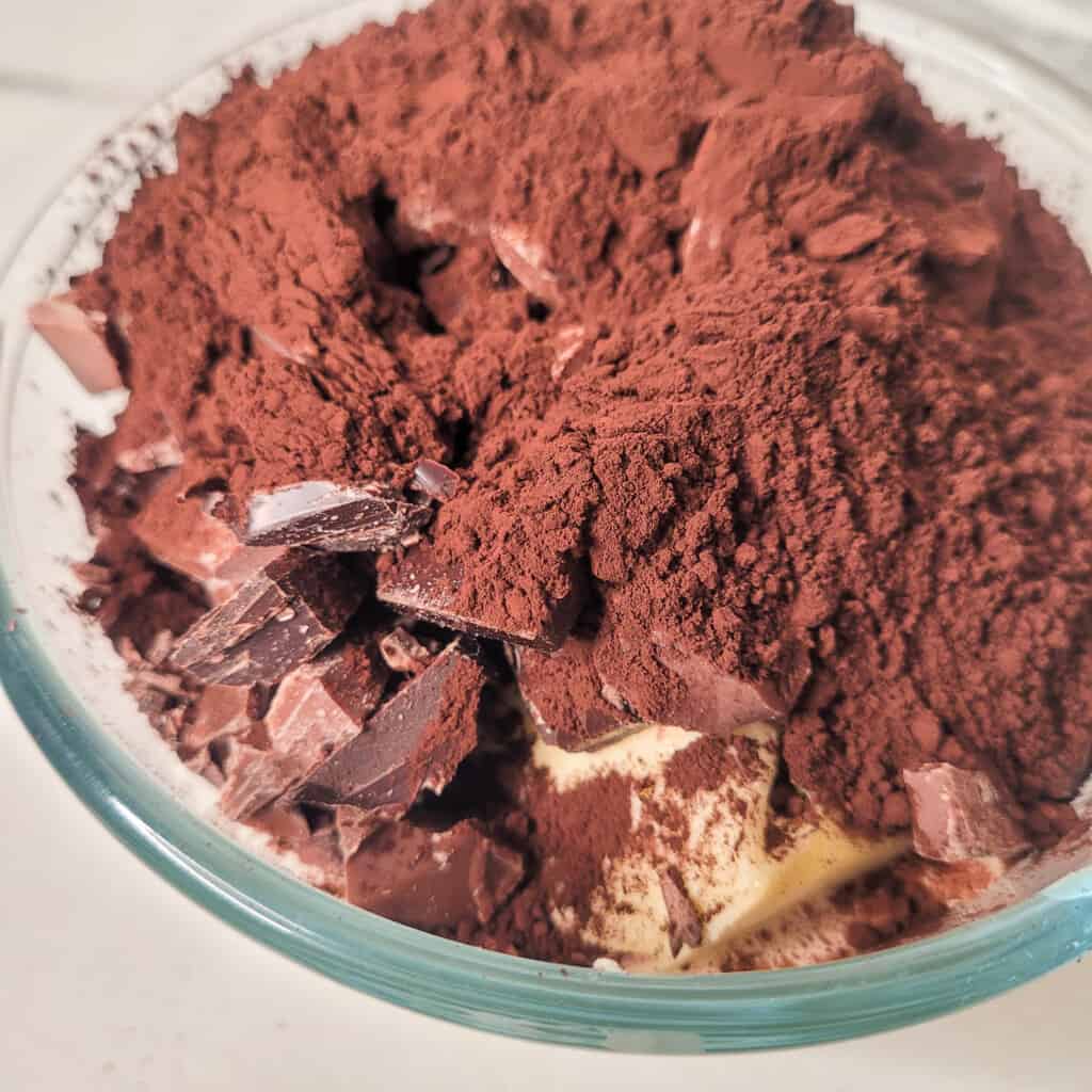 Chopped chocolate, butter, cocoa powder, instant coffee powder in a glass bowl