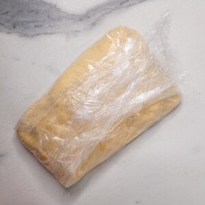 Raw pie dough shaped and covered in cling-wrap.