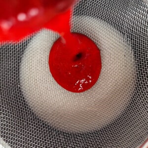Pouring pureed strawberries through a sieve into the cornstarch, water, and lemon juice mix.