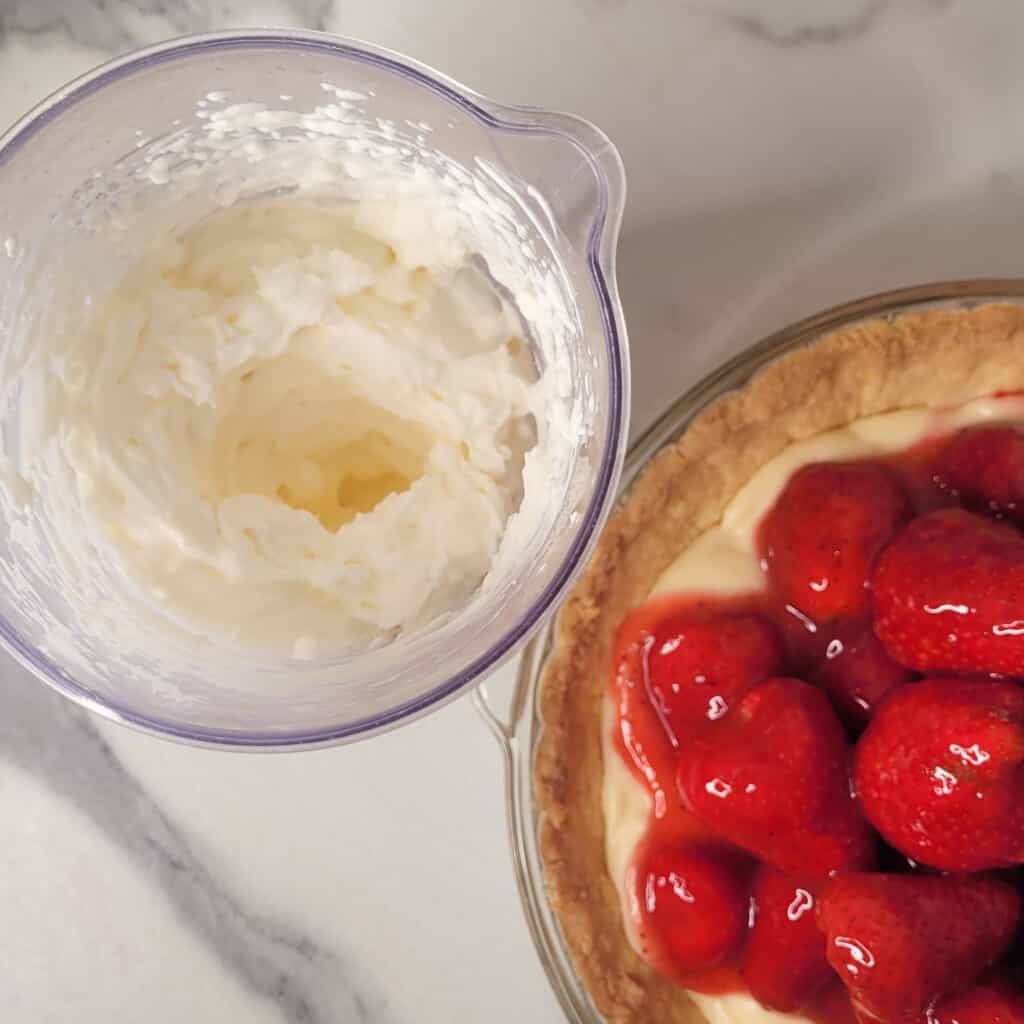 Homemade whipped cream next to strawberry custard pie.