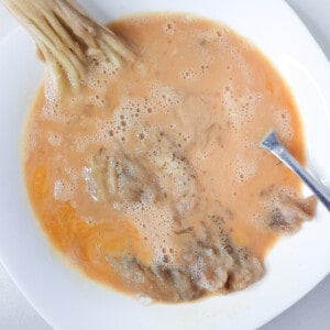 Flattened roasted eggplant in a bowl of whisked eggs