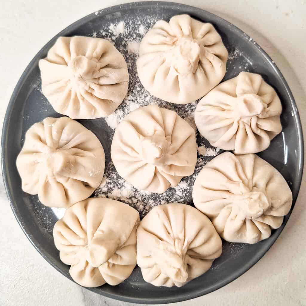 Raw, closed, and pleated khinkali pieces on a gray plate.
