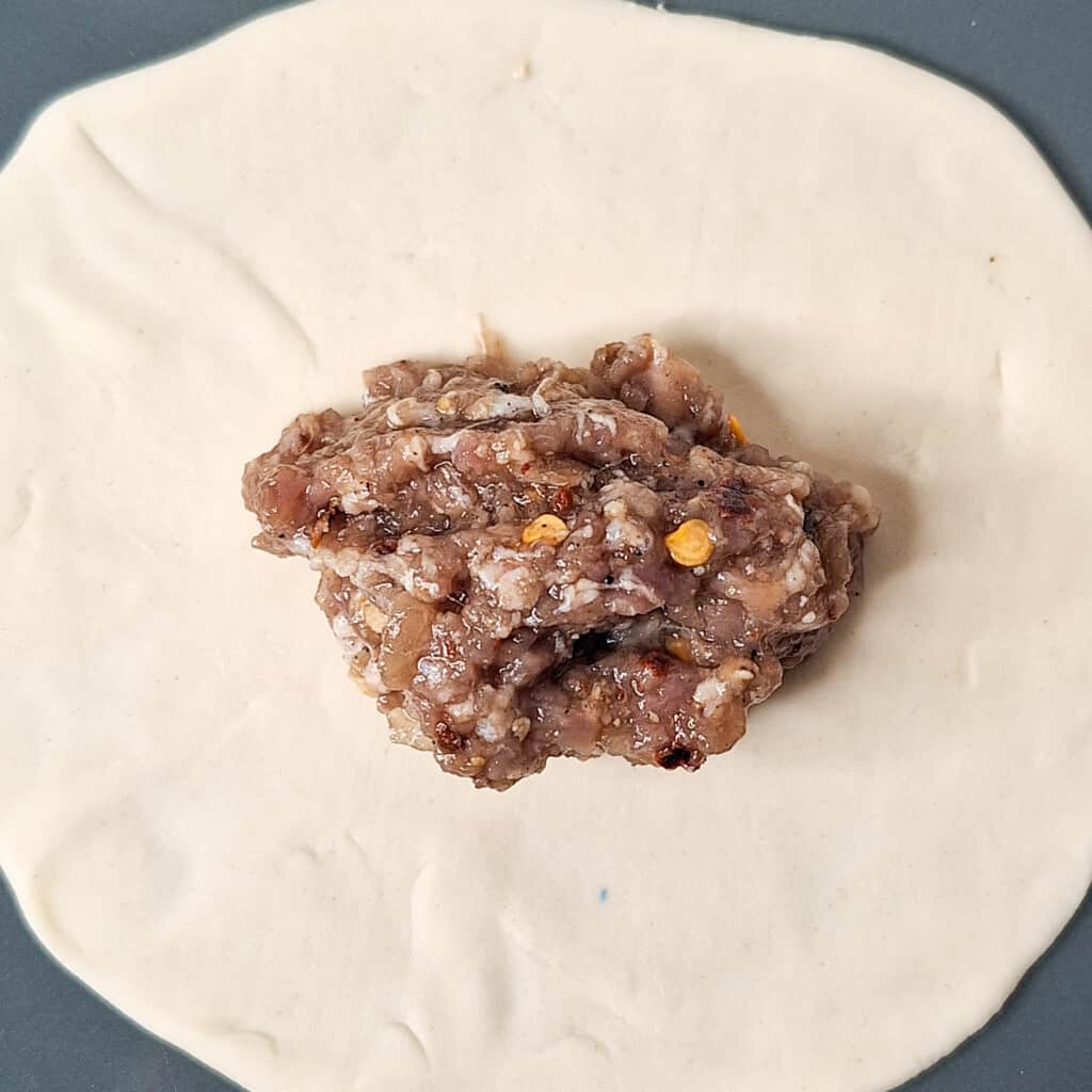 A scoop of minced meat filling in the middle of a dumpling wrapper.