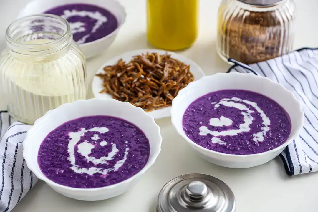 Two bowls of ube champorado or sweet rice pudding with ube flavor next to various plates of food
