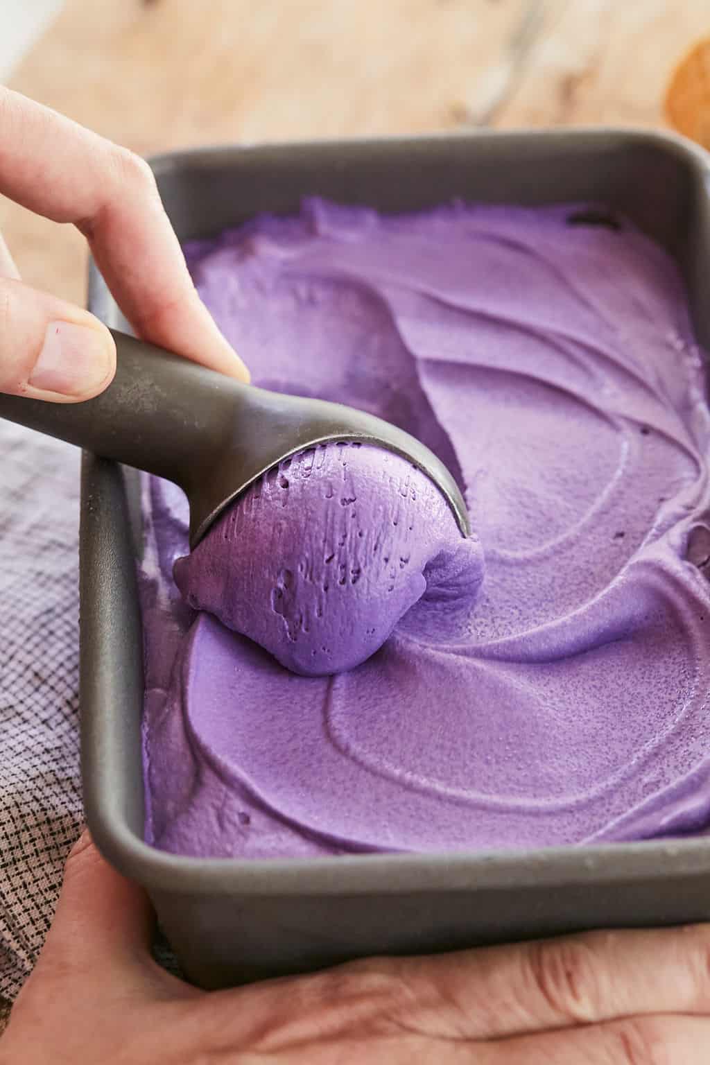 A hand scooping some ube ice cream from a container