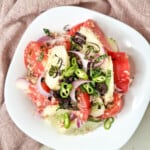 Georgian cucumber tomato salad topped with chopped chilies and purple basil in a white bowl