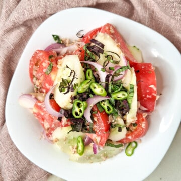 Georgian cucumber tomato salad topped with chopped chilies and purple basil in a white bowl