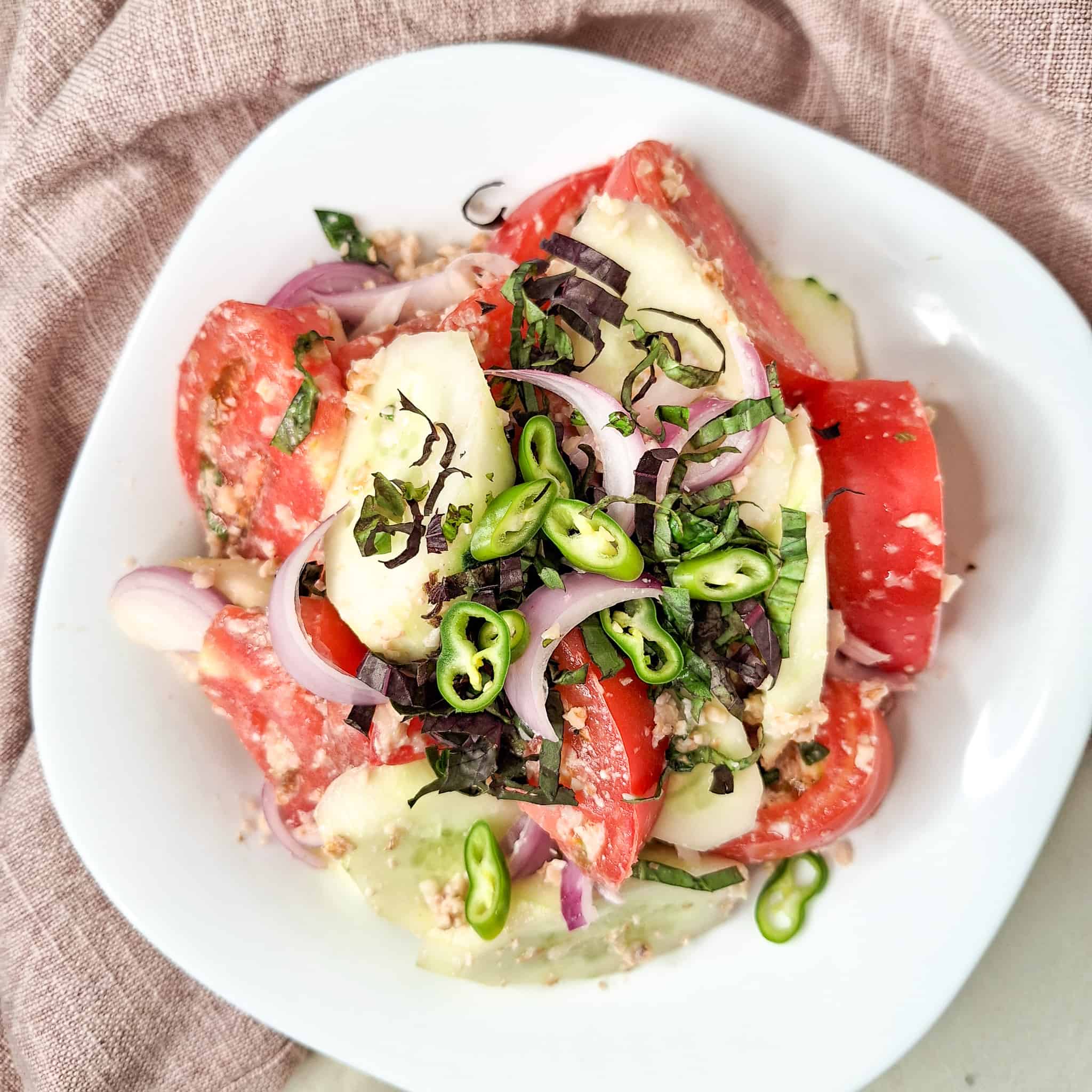 Georgian cucumber tomato salad topped with chopped chilies and purple basil in a white bowl