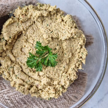 walnut paste inside a clear bowl topped with a sprig of parsley