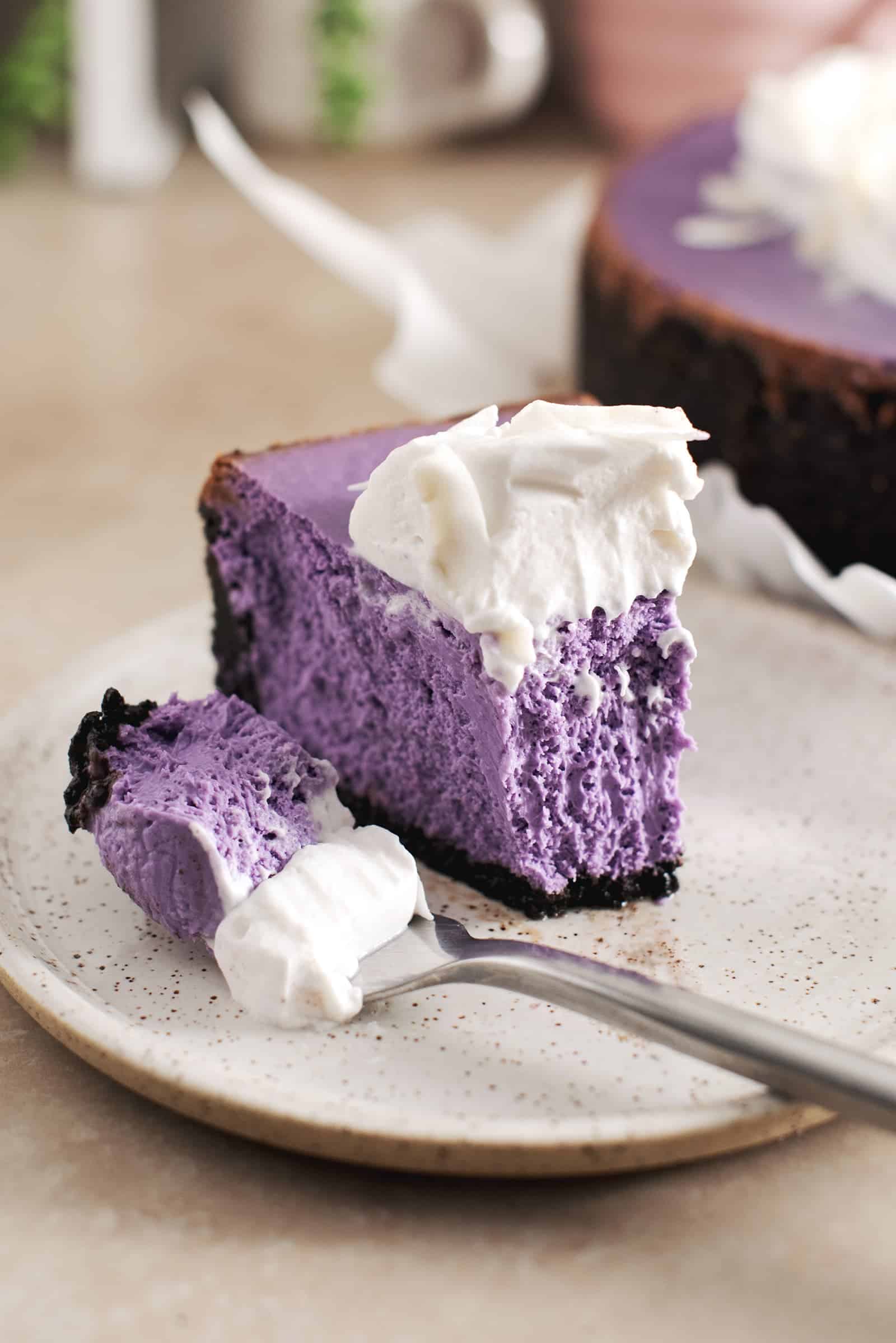 A sliced ube cheesecake next to a fork on a speckled plate