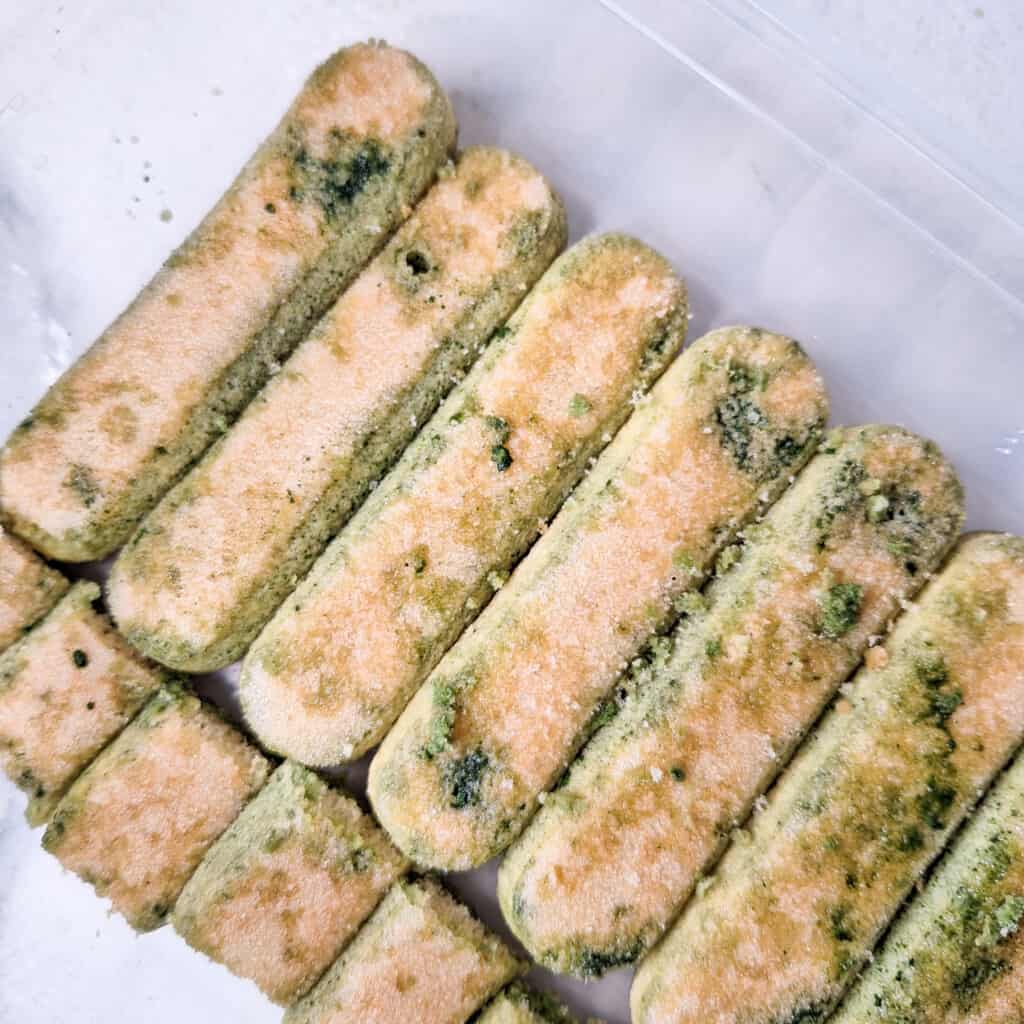 Ladyfingers dipped in matcha green tea laid out in a container