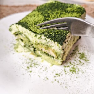 A fork slicing into a square of matcha tiramisu on a white plate