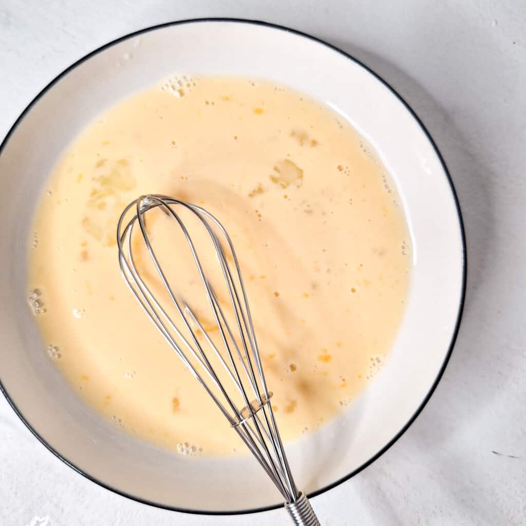 A white bowl with whisked eggs and milk
