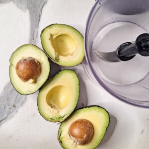 Split avocados next to an empty food processor