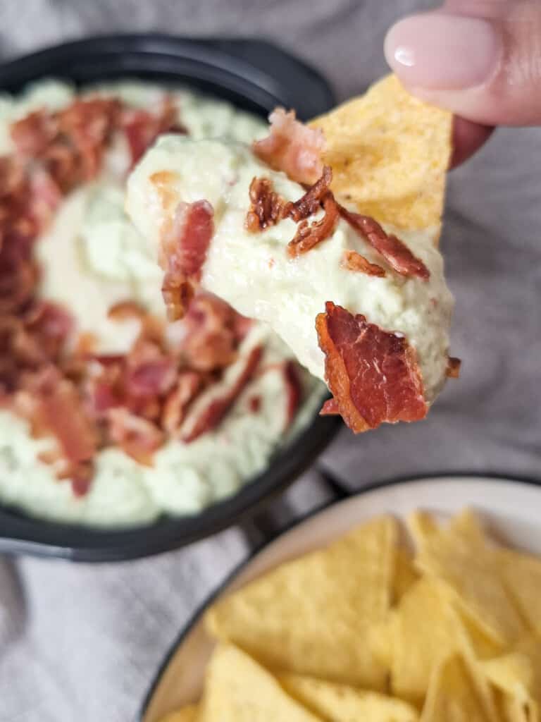 A tortilla chip with a scoop of avocado garlic dip