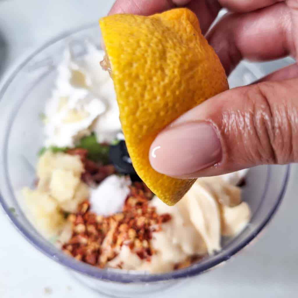 Hand squeezing a lemon over ingredients inside a food processor