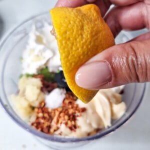 Hand squeezing a lemon over ingredients inside a food processor