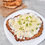 A langos or Hungarian deep fried bread with a topping of sour cream, cheese, and green onions on a white plate