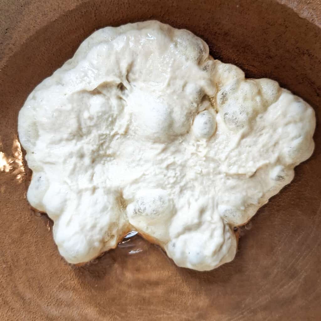Raw langos dough frying in oil