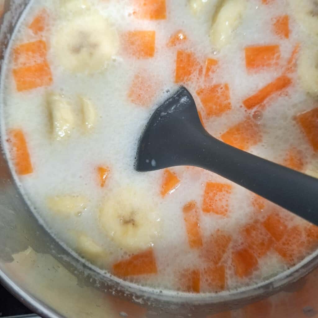 Spatula mixing a pot filled with sweet potato and bananas