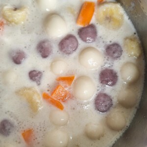 A pot filled with glutinous rice balls, sweet potatoes, and bananas in coconut milk