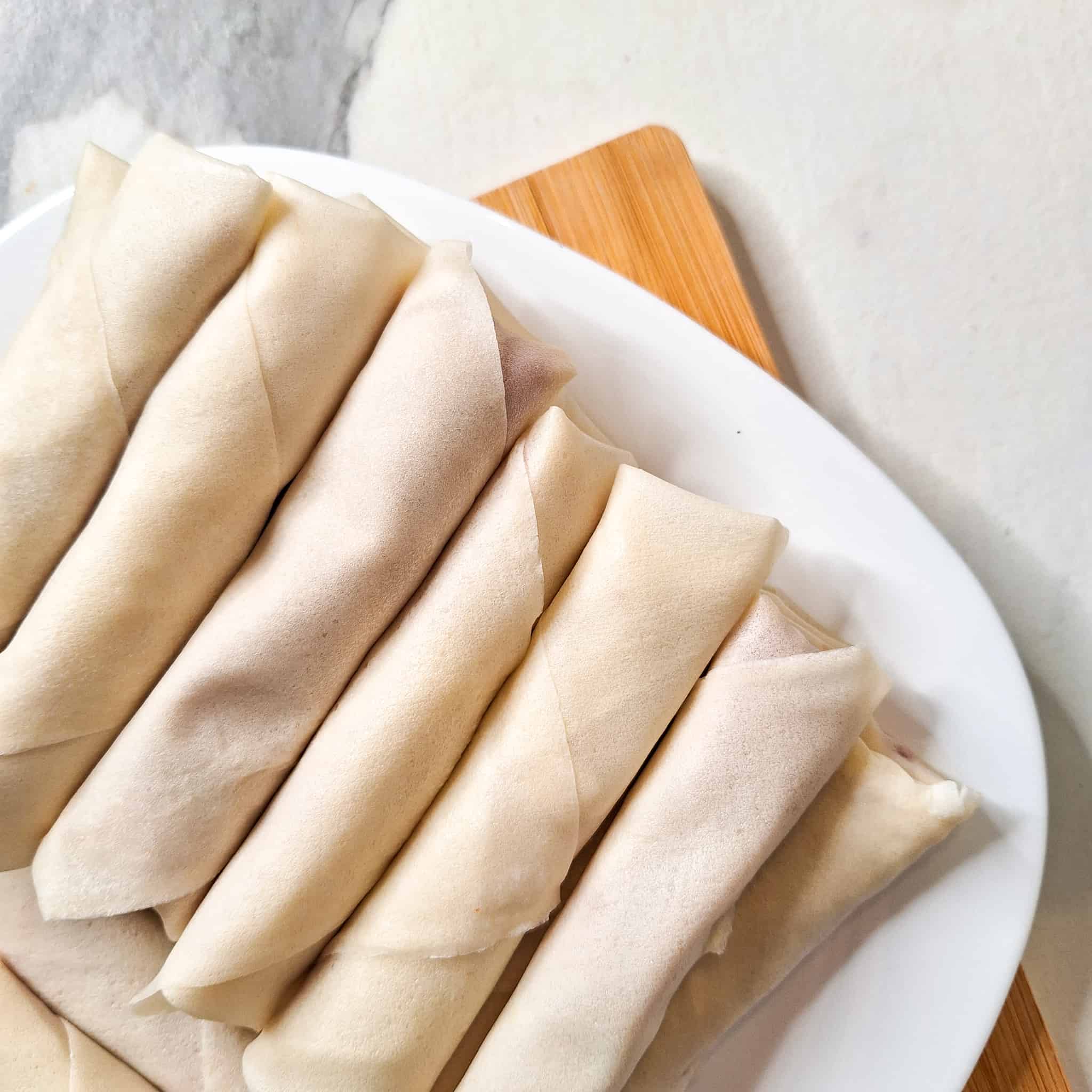 A plated of rolled lumpia on a wooden cutting boardd