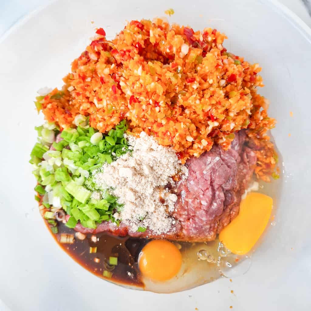 Minced vegetables, ground meat, and sauces in a plastic bowl