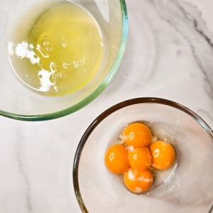 Two glass bowls, one with egg whites and the other with egg yolks next to each other