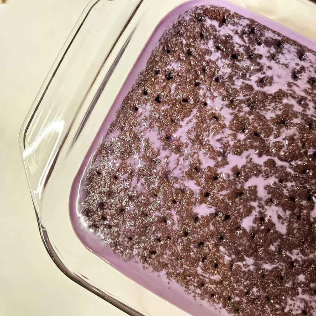 Soaking ube tres leches cake in a glass baking dish