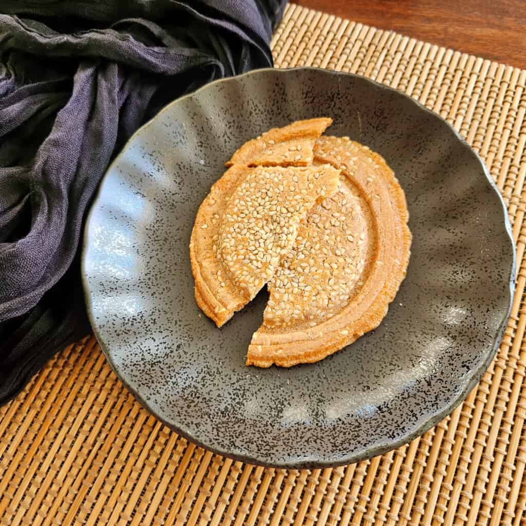 A round rice cracker broken in half on a dark plate